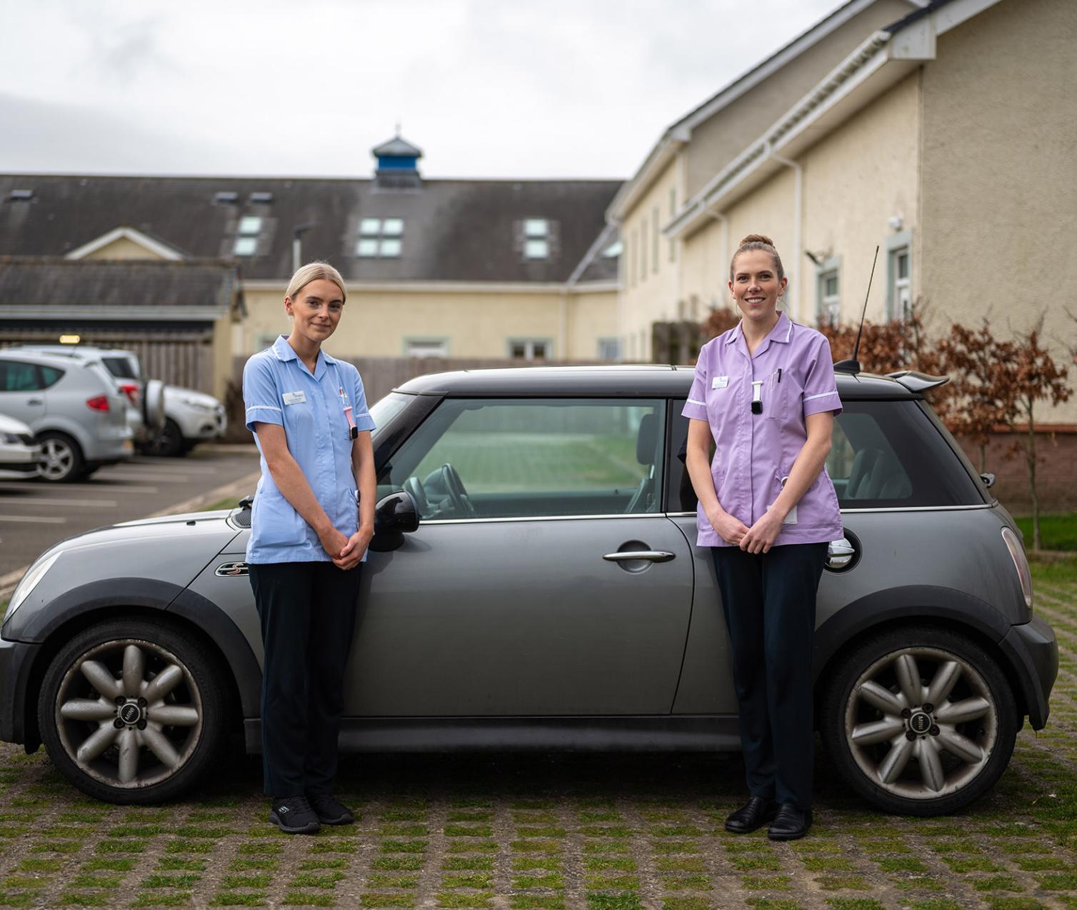 Two nurses standing by a car