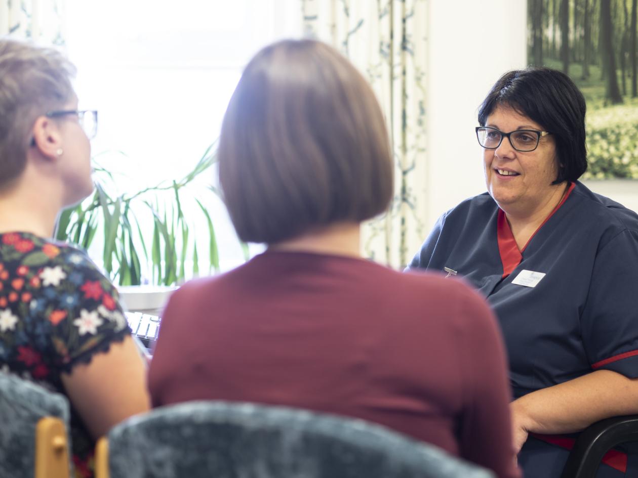 A nurse talking to a couple of people whilst sat down